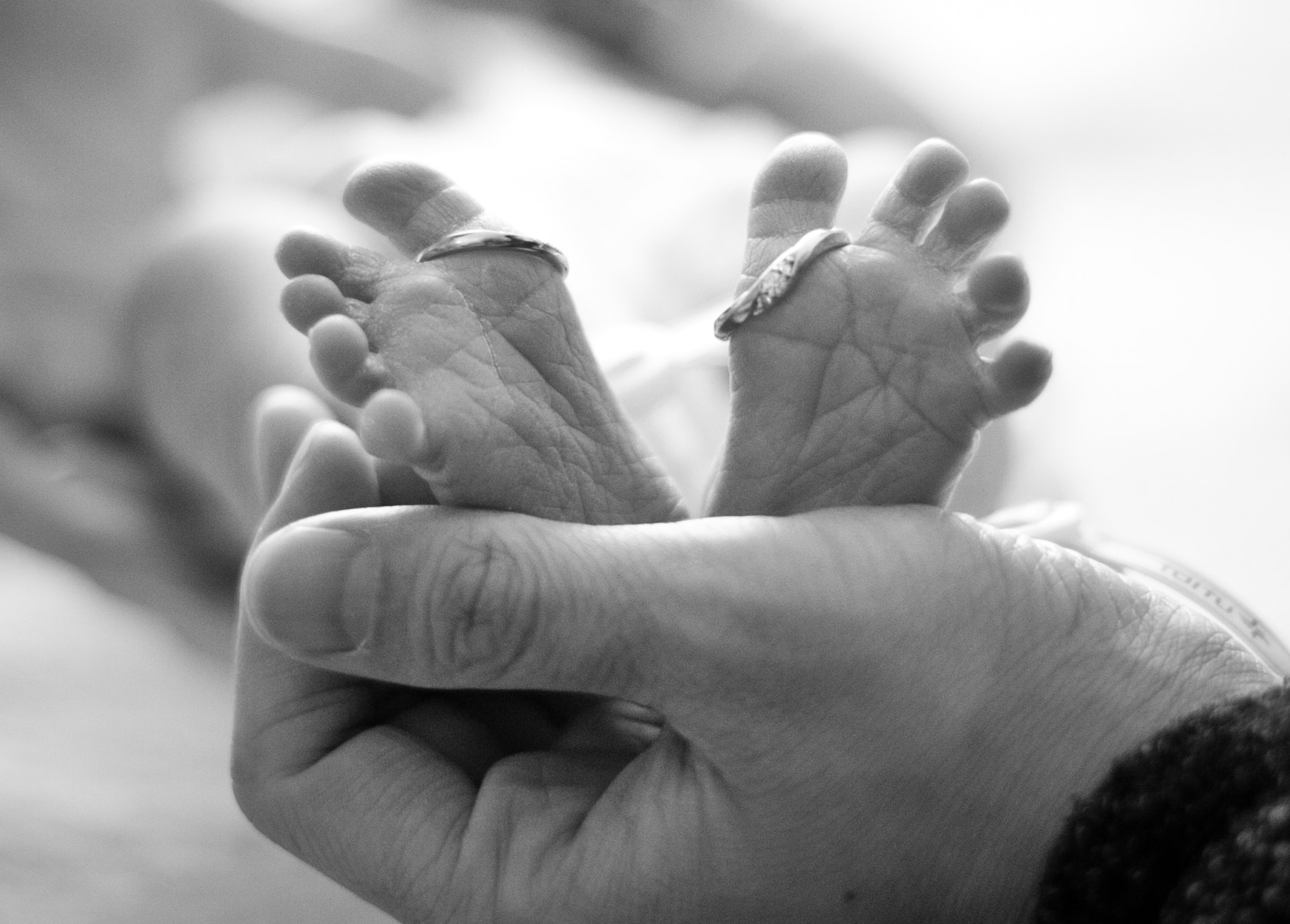赤ちゃんの足を両親の手でくるんでいるモノクロのイメージ写真